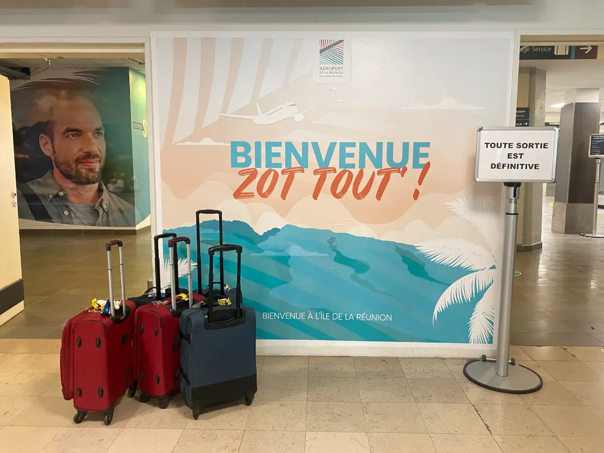 Fresque « Bienvenue zot tout' » dans le hall d'arrivée de l'aéroport de La Réunion Roland Garros, avec des valises au premier plan
