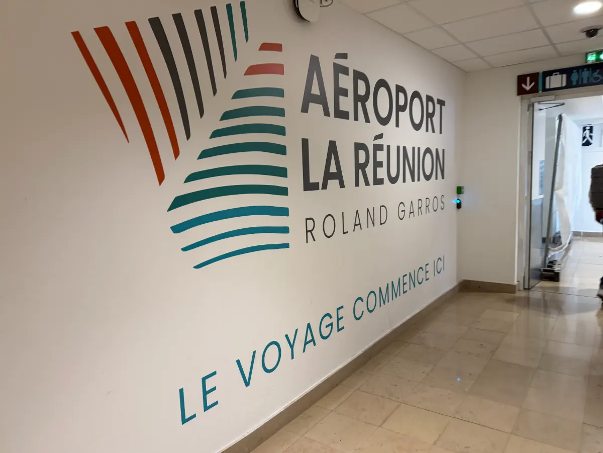 Signalétique murale de l'aéroport de La Réunion Roland Garros avec la mention « le voyage commence ici », dans un couloir menant à la livraison des bagages