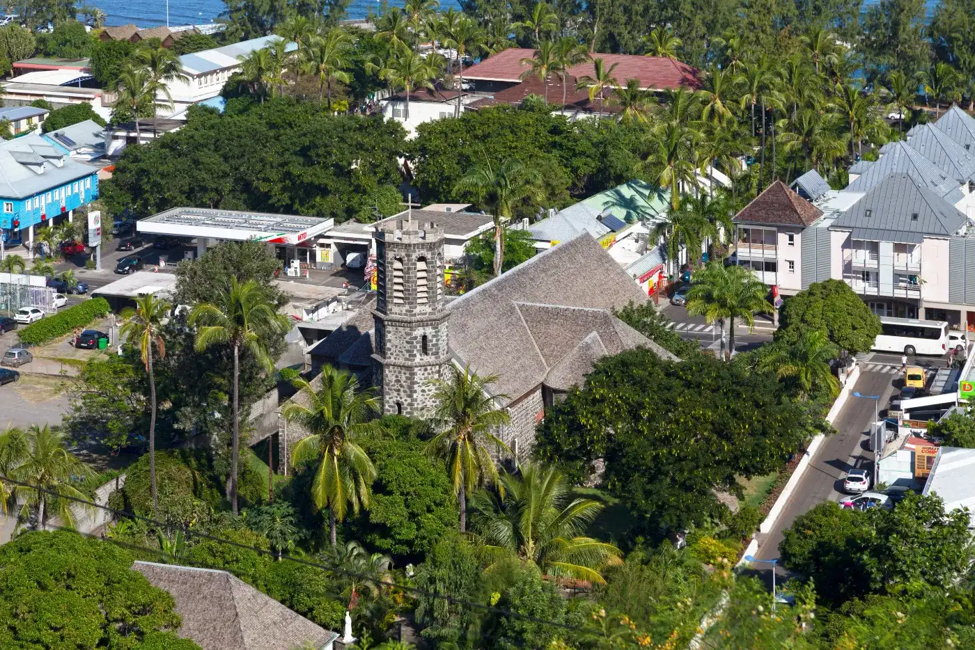 Vue aérienne d'un bourg créole de La Réunion : église en pierre de taille, toitures de tôle, cocotiers et océan en arrière-plan
