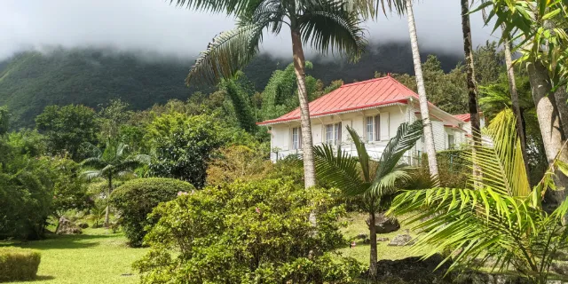 Case créole au toit rouge dans un jardin tropical, au pied des remparts des Hauts de La Réunion