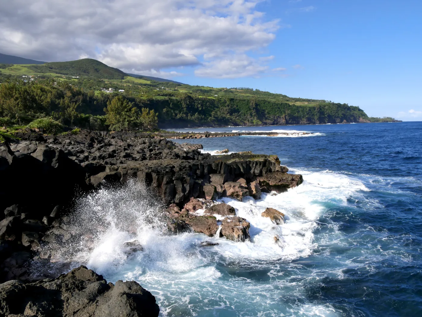 Houle se brisant sur les coulées de basalte du littoral sauvage de Saint-Philippe, avec les pentes cultivées en arrière-plan