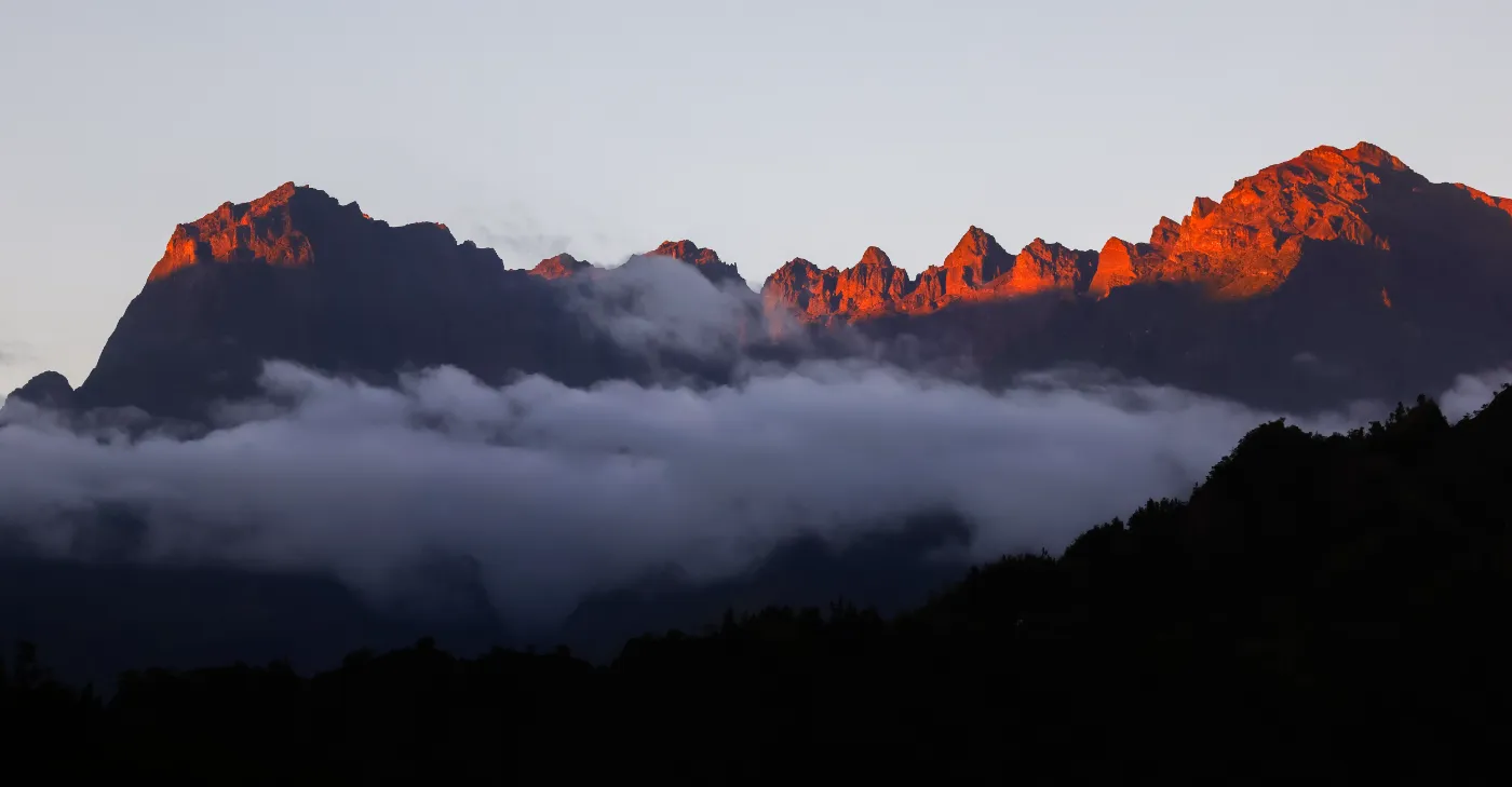 Les remparts d'un cirque de La Réunion embrasés par le lever du soleil, au-dessus d'une mer de nuages